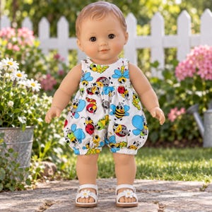 May include: A doll with light brown hair and brown eyes wearing a white sleeveless romper featuring a colorful pattern of cartoon insects including bees, ladybugs, and caterpillars, paired with white sandals adorned with small white daisy flowers.