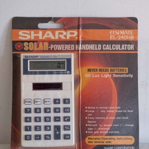 May include: A white Sharp Elsi Mate EL-240HB solar-powered handheld calculator with a black display and grey buttons. The packaging features the text "NEVER NEEDS BATTERIES" and "50 Lux Light Sensitivity".