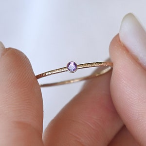 Könnte beinhalten: Ein zarter Goldring mit einem kleinen, hellvioletten Edelstein.
