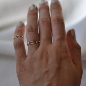 Könnte beinhalten: Eine Hand trägt zwei goldene Ringe am Zeige- und Mittelfinger. Die Hand trägt auch ein goldenes Kettenarmband am Handgelenk.