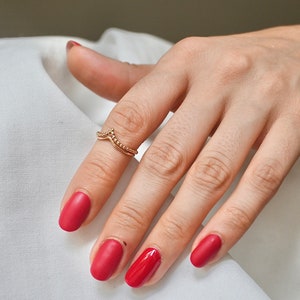 Könnte beinhalten: Eine Hand mit rotem Nagellack trägt zwei goldene Ringe am Mittelfinger. Die Ringe sind dünn und zart, mit einem Perlenmuster.