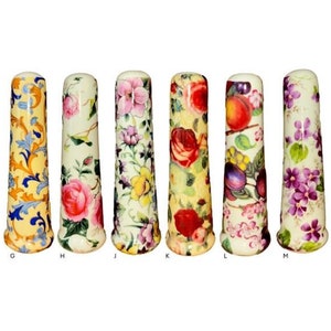 May include: Six ceramic bottle stoppers with different floral and fruit designs. The stoppers are white with yellow, blue, pink, and purple accents.