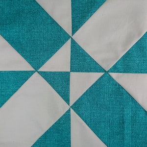 Puede incluir: Una colcha con un patrón geométrico de cuadrados y triángulos blancos y azul verdoso alternados.