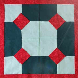 Pode incluir: Um bloco de colcha com um esquema de cores vermelho, branco e verde escuro. O bloco é composto por quadrados e diamantes, e o design é simétrico.