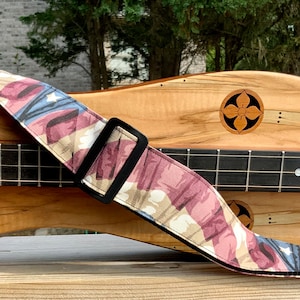 Puede incluir: Primer plano de un instrumento musical de madera con una correa de guitarra estampada. La correa presenta un diseño rojo, blanco y azul.