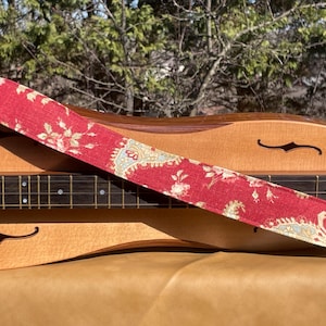 Puede incluir: Una correa de guitarra con estampado floral rojo y blanco sobre una guitarra acústica de madera.