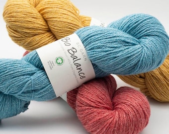 May include: Three skeins of BC Garn Bio Balance yarn in mustard yellow, light blue, and muted red. Each skein features a white paper label with the text Bio Balance, 55% Organic Wool / 45% Pure Organic Cotton, and organic certification.