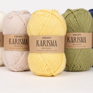 May include: Five skeins of Drops Karisma Uni Colour yarn in various colors: cream, light beige, yellow, olive green, and navy blue. Each skein has a brown paper label with the brand name and product details.