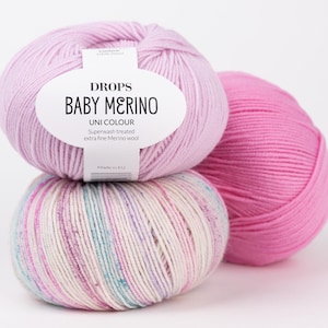May include: Three balls of yarn stacked together. The top ball is light pink with a white label reading DROPS BABY MERINO UNI COLOUR. The bottom ball is white with pink and blue speckles. The third ball is a solid bright pink colour.