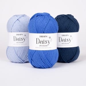 May include: Three skeins of Drops Daisy yarn in shades of light blue, medium blue, and dark navy blue. Each skein features a white paper label with the text Drops Daisy Uni Colour 100% extra fine merino wool printed in black ink.