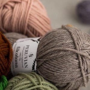 May include: A close-up of four balls of yarn in various colors: brown, gray, pink, and green. The yarn is labeled 'PERUVIAN filcolana'.