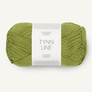 May include: A skein of green yarn with a white label. The label reads "TYNN LINE" with the brand name "SANDNES GARN" above it. The yarn is a light green color and appears to be soft and textured. The yarn is tightly wound into a ball.