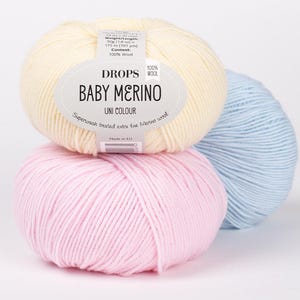 May include: Three balls of yarn in pink, light blue, and cream. The cream ball has a label that reads 'DROPS 100% WOOL BABY MERINO UNI COLOUR Superwash treated extra fine Merino wool Made in EU'.