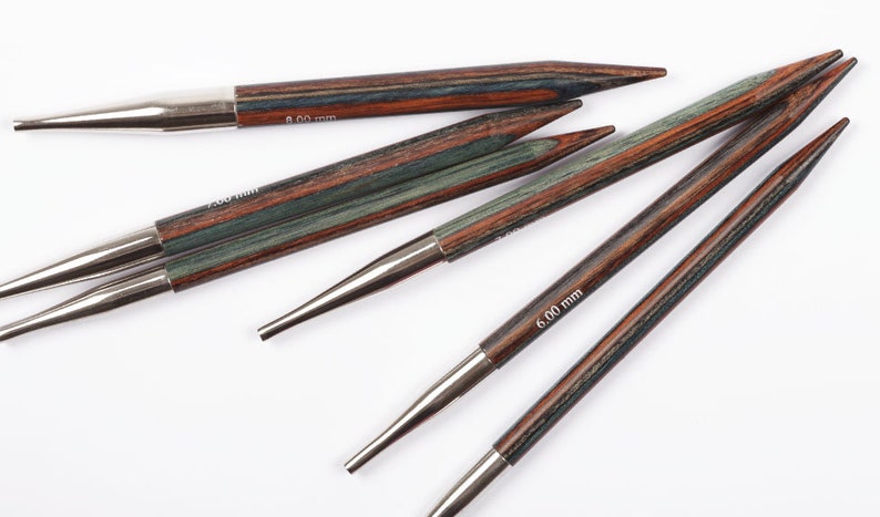 Puede incluir: Un conjunto de agujas de tejer de madera con puntas met&aacute;licas. Las agujas presentan un dise&ntilde;o a rayas en tonos marr&oacute;n, verde y rojo. Los tama&ntilde;os est&aacute;n indicados en las agujas como 6,00 mm y 8,00 mm.