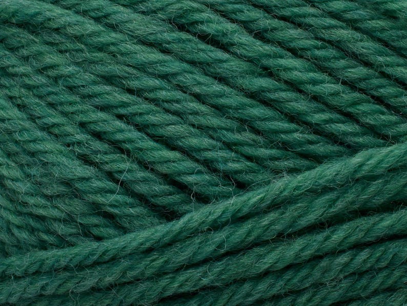 Op de afbeelding: Een close-up van donker bosgroen garen, met de getwiste vezelstructuur en de zachte, pluizige textuur van de individuele draden. Het garen is in parallelle rijen gerangschikt, wat de diepe, rijke kleur en de consistente draadstructuur benadrukt.