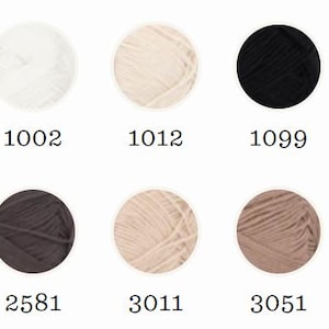 May include: A collection of yarn skeins in various colors, including white, cream, black, and brown. Each skein is labeled with a number, and one is marked "NEW". The yarn is arranged in a grid, showcasing the range of available shades.