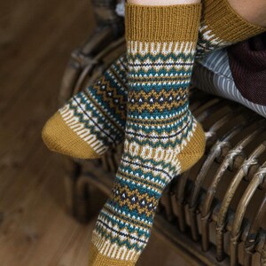 May include: A pair of warm, cozy socks with a geometric pattern in shades of mustard yellow, teal, white, and black. The socks are made of a soft, knitted fabric.
