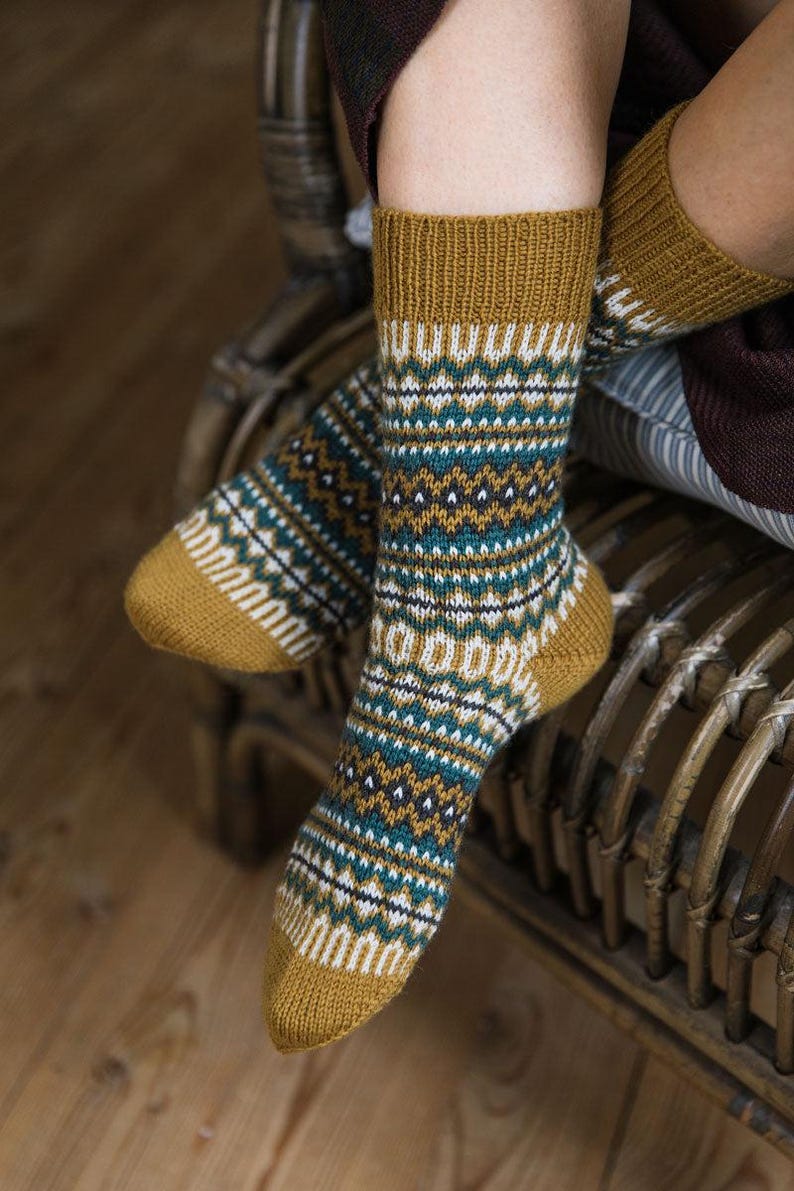May include: A pair of warm, cozy socks with a geometric pattern in shades of mustard yellow, teal, white, and black. The socks are made of a soft, knitted fabric.