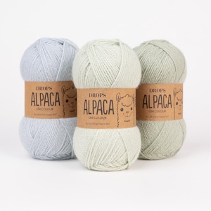 May include: Three skeins of yarn in light blue, pale mint green, and sage green. Each skein features a brown paper label with the text DROPS ALPACA UNI COLOUR and a line drawing of an alpaca face, wrapped around the center of the yarn ball.