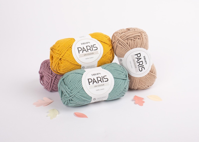May include: Four balls of Drops Paris yarn in different colors: yellow, green, beige, and purple. The yarn is 100% cotton and is labeled 'Drops Paris Uni Colour'.