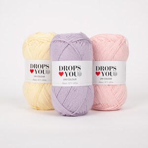 Puede incluir: Tres ovillos de hilo Drops You Uni Colour en tonos pastel: amarillo p&aacute;lido, lavanda y rosa claro. Cada ovillo tiene una etiqueta blanca con el texto "DROPS YOU" y "UNI COLOUR". El hilo es de algod&oacute;n cl&aacute;sico 8/4.