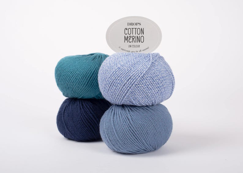 Puede incluir: Cuatro ovillos de lana apilados en dos columnas, con tonos verde azulado, azul marino oscuro, azul claro y azul medio. Una etiqueta ovalada en la parte superior muestra el texto DROPS COTTON MERINO UNI COLOUR, un hilo superwash.