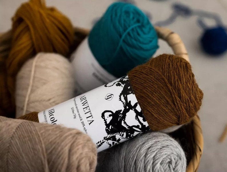 May include: A close-up of a brown ball of yarn with a white label that reads 'Arwetta Superwash Merino Wool & 20% nylon 210m - 50g Filcolana'.