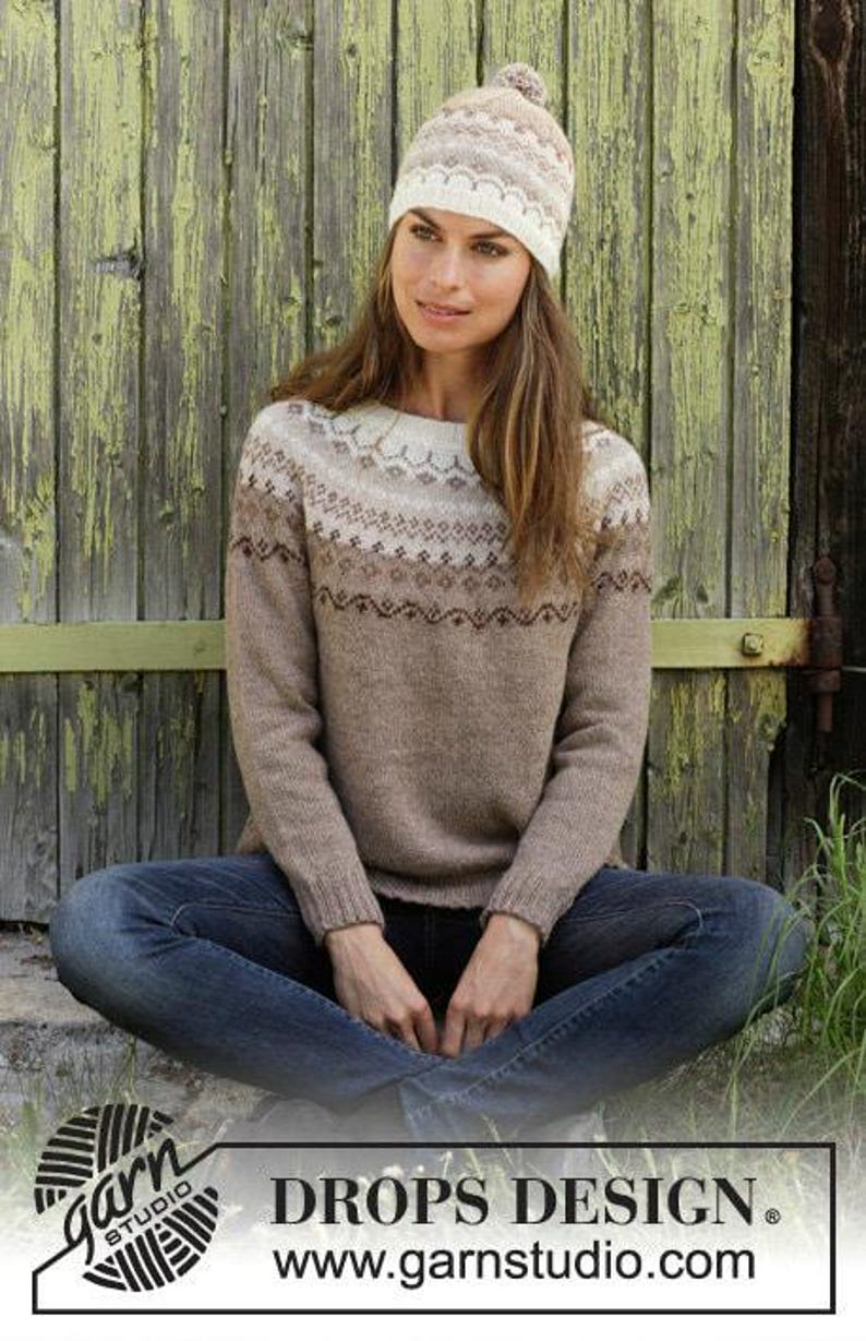 May include: A beige and white long-sleeve knit sweater with a round neckline and a fair isle pattern across the chest and shoulders, paired with a matching knit beanie featuring a pom-pom and blue denim jeans.
