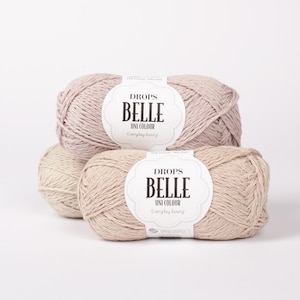 May include: Several skeins of Drops Belle Uni Colour yarn in neutral tones, including beige and light pink. Each skein has a white label with black text. The yarn is arranged on a white background, ideal for knitting and crochet projects.