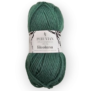 Op de afbeelding: Een bol donkergroen garen met een wit papieren label. Het label bevat de tekst PERUVIAN, 100% peruvian highland wool, 100m/50g en filcolana, samen met de zin OBSESSED WITH QUALITY YARN SINCE 1952 in zwarte letters.