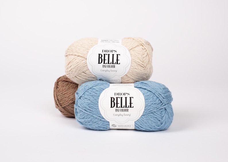 May include: Three skeins of Drops Belle Uni Colour yarn in beige, brown, and blue. Each skein has a label with the brand name and product details. The yarn is arranged in a stack against a white background.