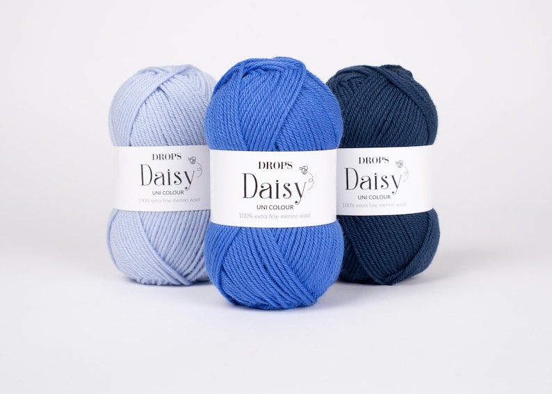 May include: Three skeins of Drops Daisy yarn in shades of light blue, medium blue, and dark navy blue. Each skein features a white paper label with the text Drops Daisy Uni Colour 100% extra fine merino wool printed in black ink.