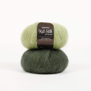 May include: Two balls of Drops Kid-Silk Uni Colour yarn, one light green and one dark green, stacked on top of each other. The top ball has a brown label with white text. The yarn appears soft and fluffy.