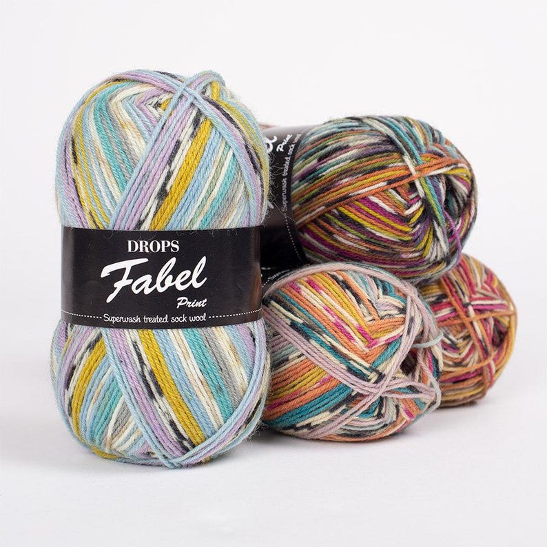 May include: Three balls of Drops Fabel Print yarn. The yarn is a superwash treated sock wool and is multicolored with shades of blue, yellow, orange, pink, green, brown, and black. The label on the yarn reads 'DROPS Fabel Print Superwash treated sock wool.'
