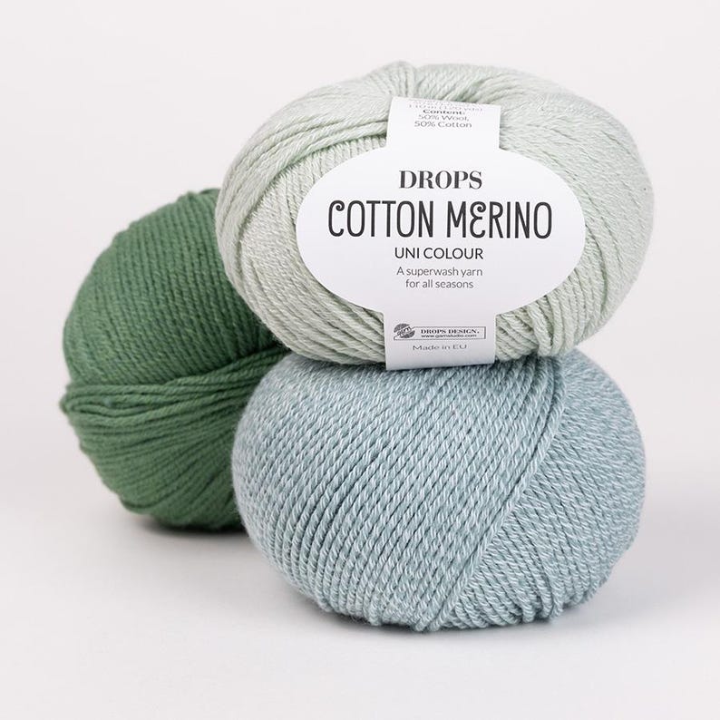 May include: Three balls of Drops Cotton Merino yarn in shades of green and blue. The top ball is light green, the middle ball is a light blue, and the bottom ball is a darker green. The label reads "Cotton Merino Uni Colour".