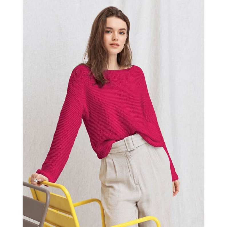 Puede incluir: Un su&eacute;ter de punto rosa brillante con un ajuste holgado y mangas largas. El su&eacute;ter est&aacute; hecho de un material suave y c&oacute;modo y tiene un cuello ligeramente barco.