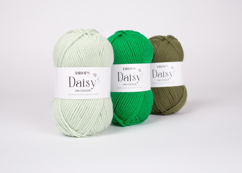 May include: Three skeins of Drops Daisy yarn arranged in a row. The first is light mint green, the second is vibrant grass green, and the third is olive green. Each skein features a white paper label with the text Drops Daisy Uni Colour.