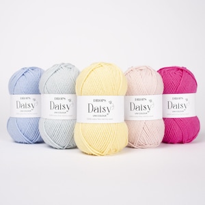 May include: Five skeins of Drops Daisy yarn arranged in a row, featuring colors of light blue, light gray, pale yellow, soft pink, and vibrant magenta. Each skein has a white paper label with the text Drops Daisy Uni Colour printed in black.