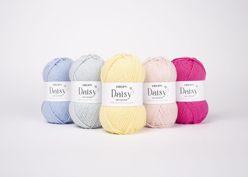 May include: Five skeins of Drops Daisy yarn arranged in a row, featuring colors of light blue, light gray, pale yellow, soft pink, and vibrant magenta. Each skein has a white paper label with the text Drops Daisy Uni Colour printed in black.