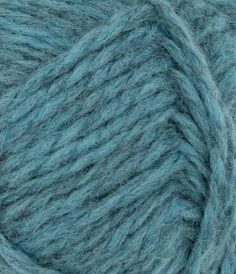 May include: A close-up view of a skein of teal blue yarn featuring a thick, fuzzy, and multi-ply twisted texture. The fibers are densely packed, creating a soft and voluminous appearance with visible individual strands woven together in a consistent pattern.