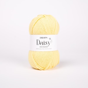 May include: A ball of pale yellow yarn with a white paper label wrapped around the center. The label features the text DROPS Daisy UNI COLOUR 100% extra fine merino wool and a small graphic of a flower. The yarn has a smooth, twisted texture.