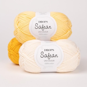 May include: Three skeins of Drops Safran Uni Colour 100% cotton yarn in shades of yellow and cream. The yarn is labeled with the brand name and product details. The skeins are arranged in a stack, with one partially visible.