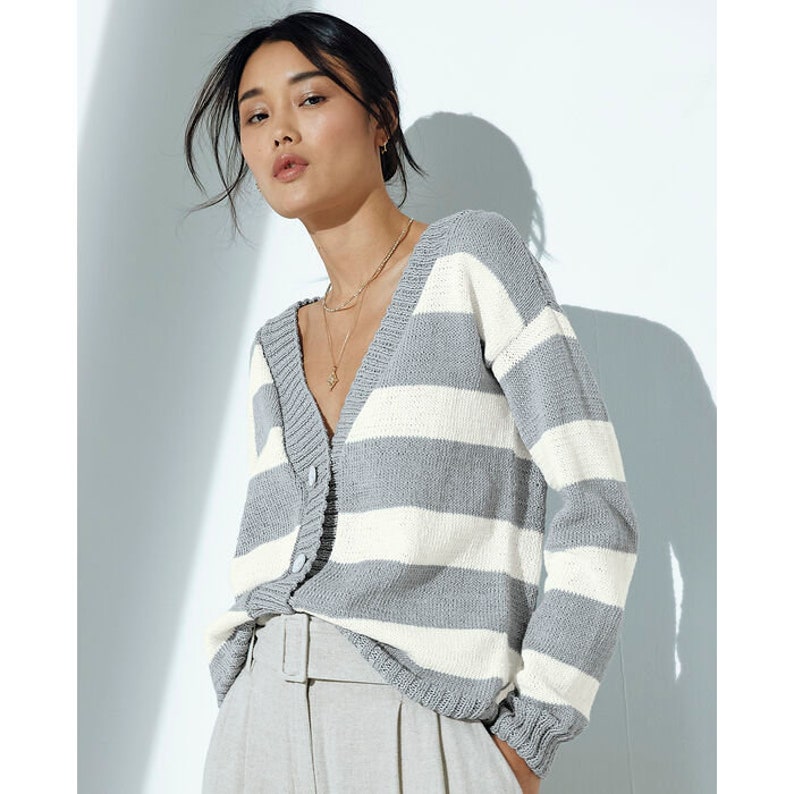 Peut inclure: Un cardigan ray&eacute; gris et blanc avec un col en V et une fermeture boutonn&eacute;e. Le cardigan est fait d'un tissu doux et tricot&eacute;.