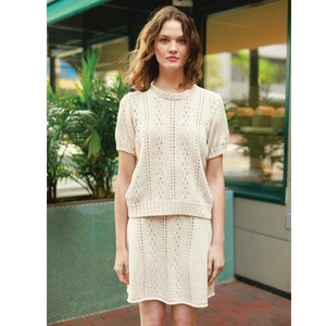 May include: A white crocheted top and skirt set with a delicate openwork pattern. The top has short sleeves and a round neckline. The skirt is knee-length and has a slightly flared silhouette.