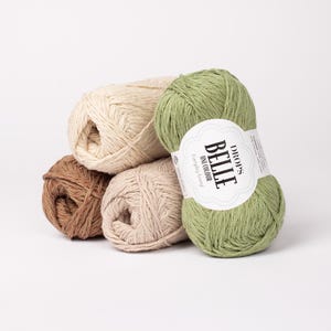 May include: A collection of yarn skeins in various colors, including brown, beige, and green. One skein has a label that reads "DROPS BELLE uni colour". The yarn is arranged on a white background.