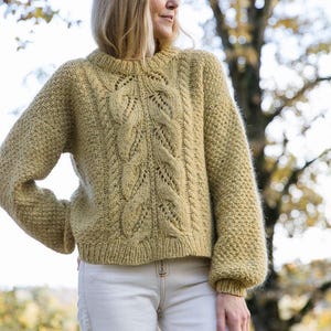 May include: A light yellow knitted sweater with a cable knit pattern and a round neckline. The sweater has a relaxed fit and is made of a soft, fuzzy yarn.