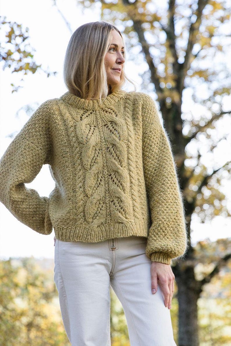 May include: A light yellow knitted sweater with a cable knit pattern and a round neckline. The sweater has a relaxed fit and is made of a soft, fuzzy yarn.