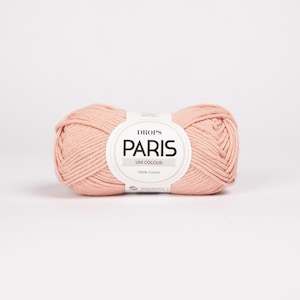 K&ouml;nnte beinhalten: Ein Kn&auml;uel Drops Paris Uni Colour Garn in einem zarten, hellrosa Farbton. Das Garn besteht aus 100 % Baumwolle und hat ein Etikett mit Markennamen und Produktinformationen. Geeignet f&uuml;r Strick- und H&auml;kelprojekte.