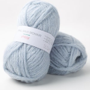 May include: Two light blue yarn balls with a soft, fluffy texture. The yarn is labeled "PHIL MAXI MOHAIR" with the brand name "phildar" visible. The label also lists the yarn's composition: 40% Acrylic, 30% Polyamide, and 30% Mohair.