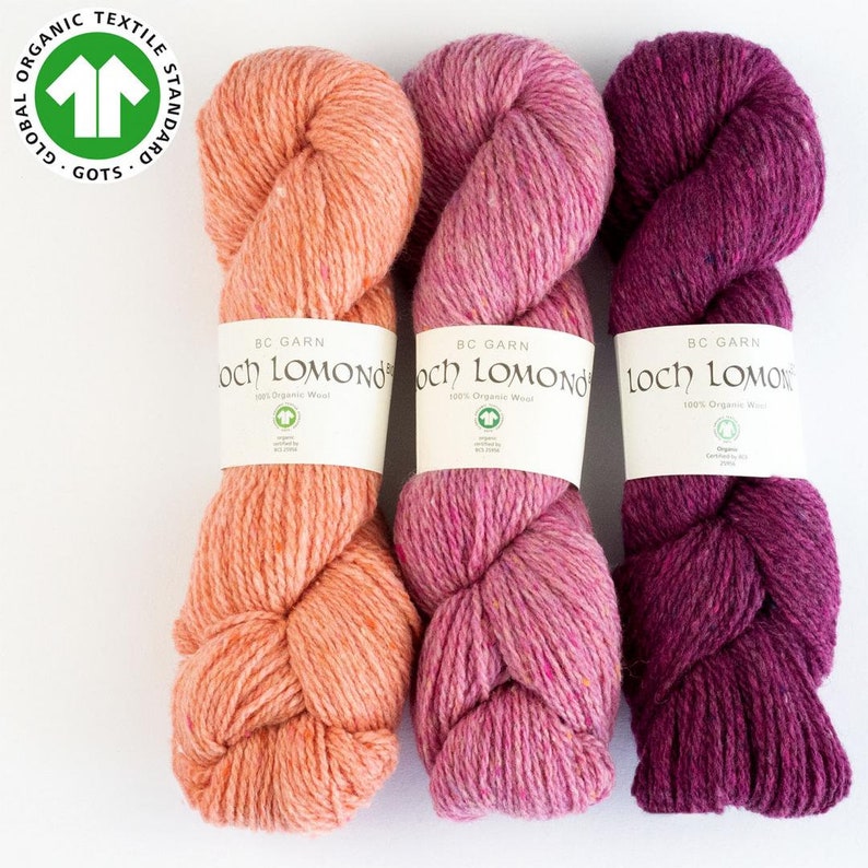 May include: Three skeins of yarn in shades of peach, pink, and burgundy. The yarn is labeled "Loch Lomond" and is 100% organic wool.